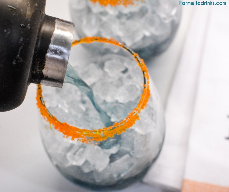 Pouring purple rain from cocktail shaker to ice filled glass with orange sugar rim.