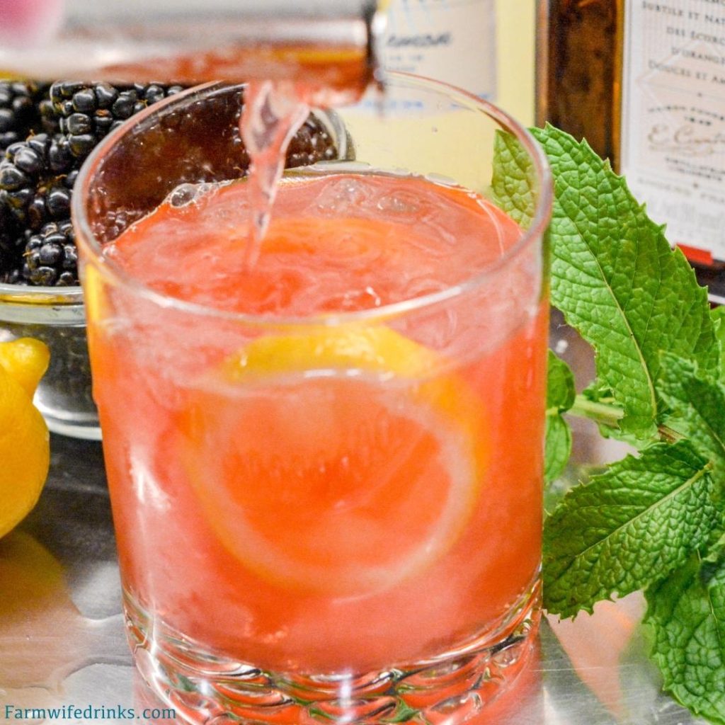 The Lily Oaks drink is a combination of cranberry juice, orange liqueur, lemonade, and vodka combined and garnished with mint, lemon, and blackberries.