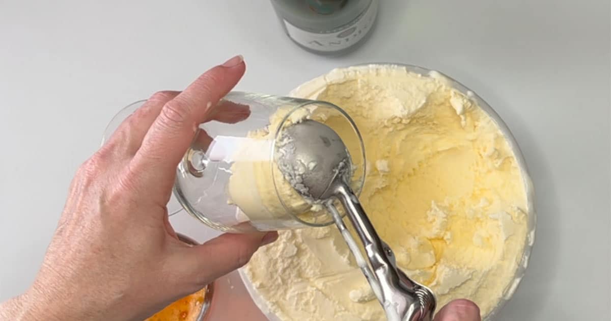 Adding scoops of ice cream into glass for the Creamsicle Mimosa Float.