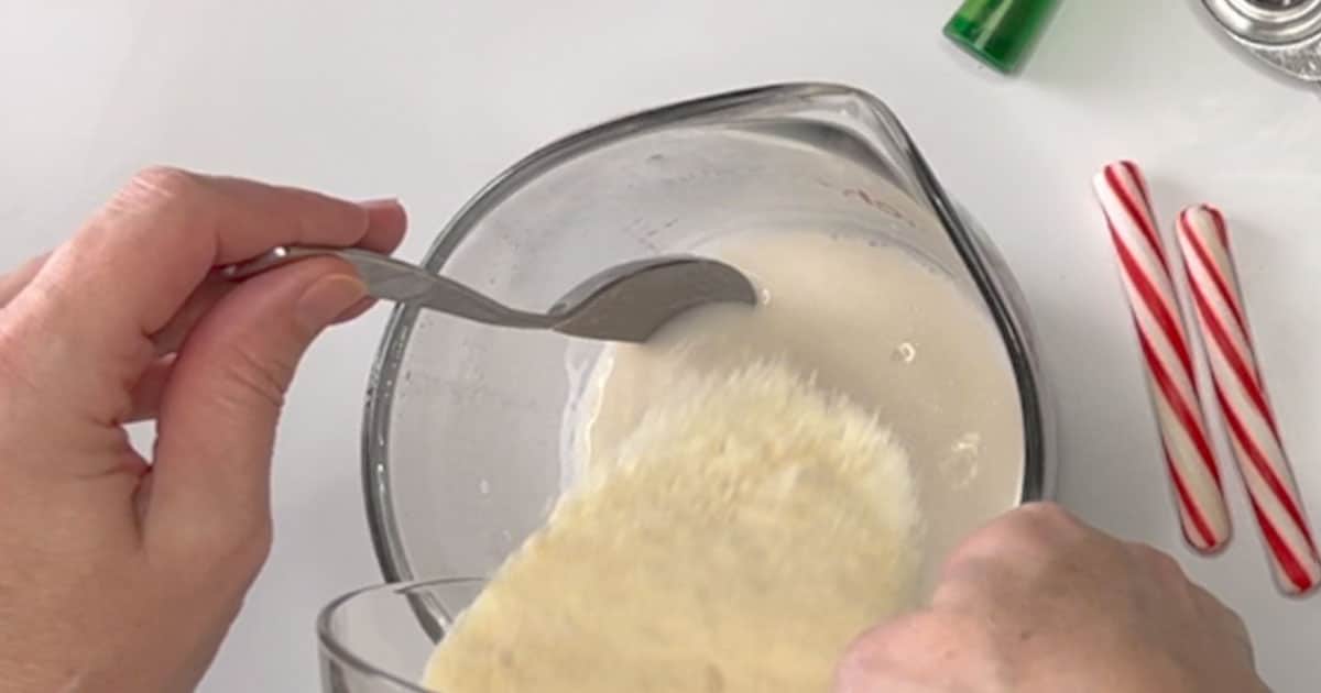 pouring in White cocoa mix into milk, for Grinch Hot Cocoa.