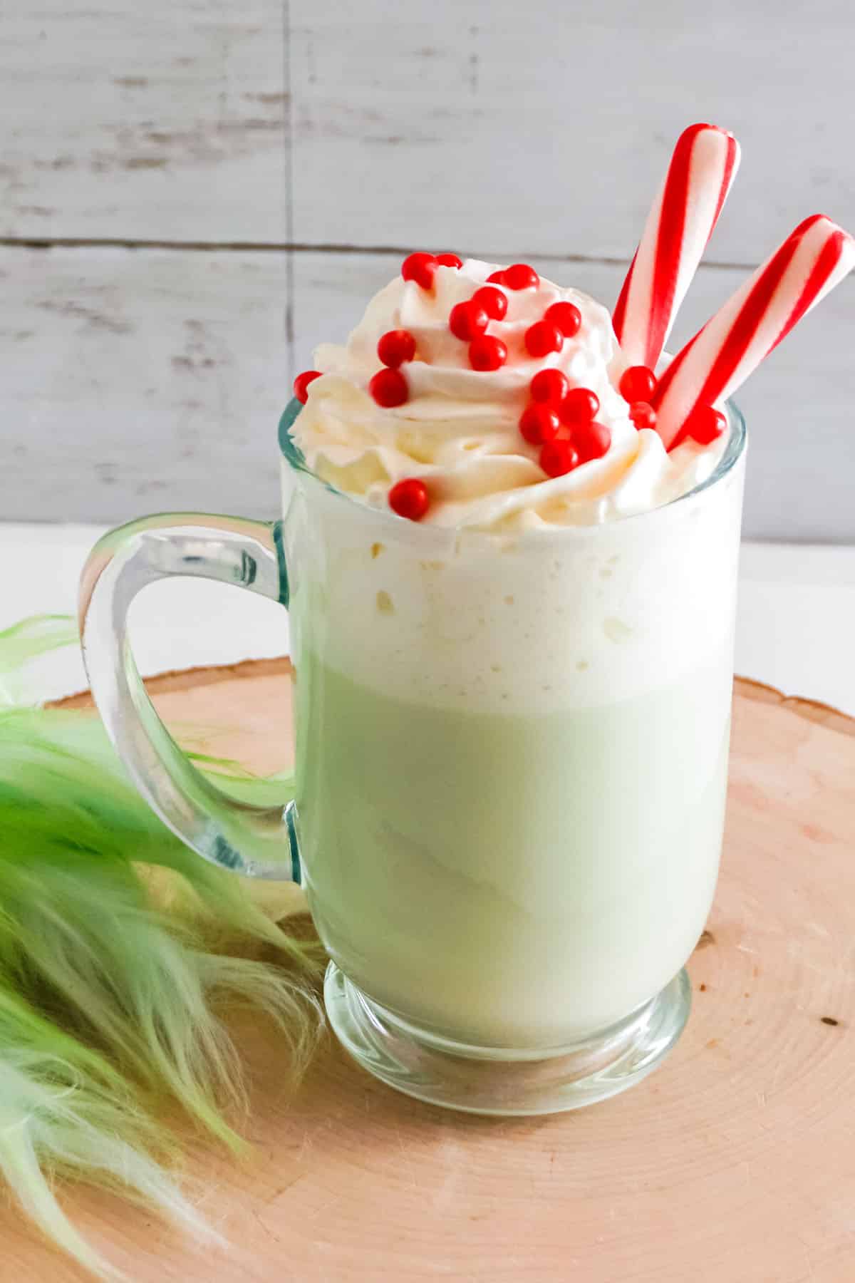 close up Grinch Hot Cocoa with Peppermints and hand on wood block.