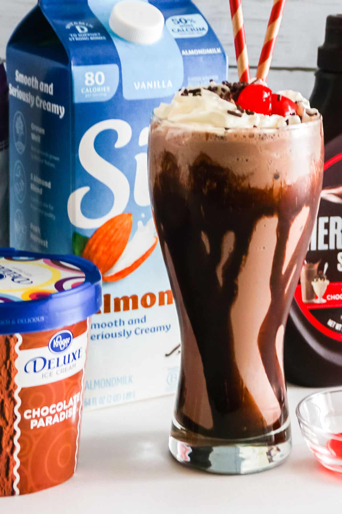 Close up of chocolate Milkshake with ingredients behind it.